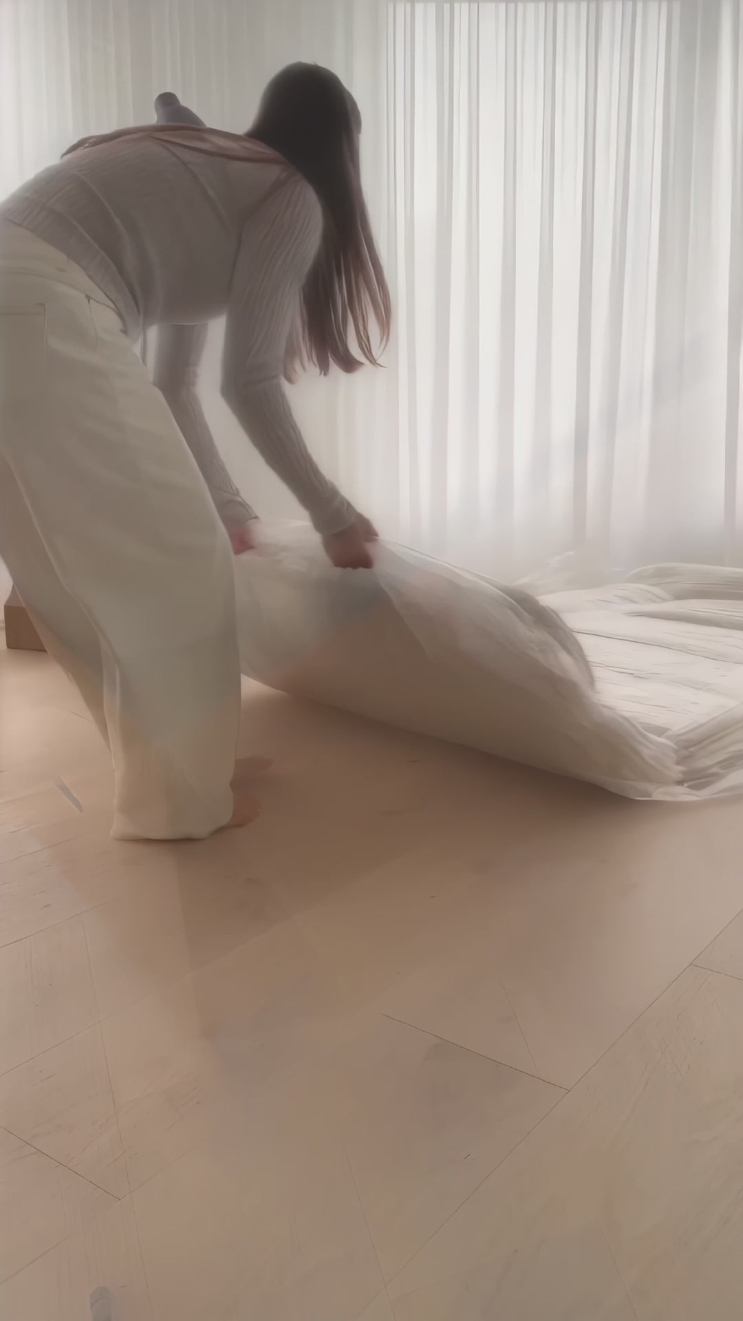 Une jeune femme déballe un canapé roulé et compressé sous vide puis l'essaye. Il est en bouclette beige et fait 2m14.