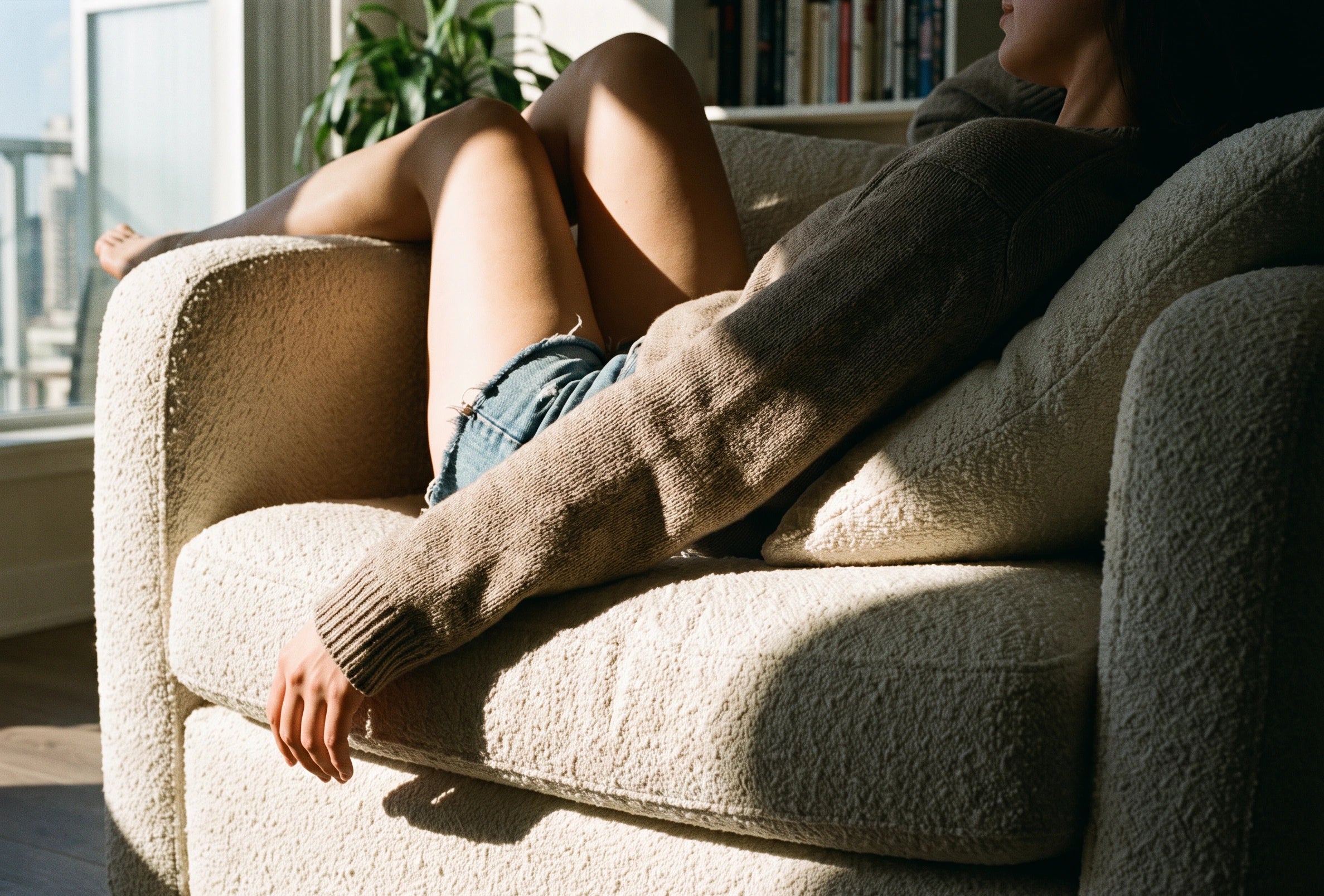 Personne allongée les jambes repliées sur le canapé Dune en bouclette écrue dans un salon Image